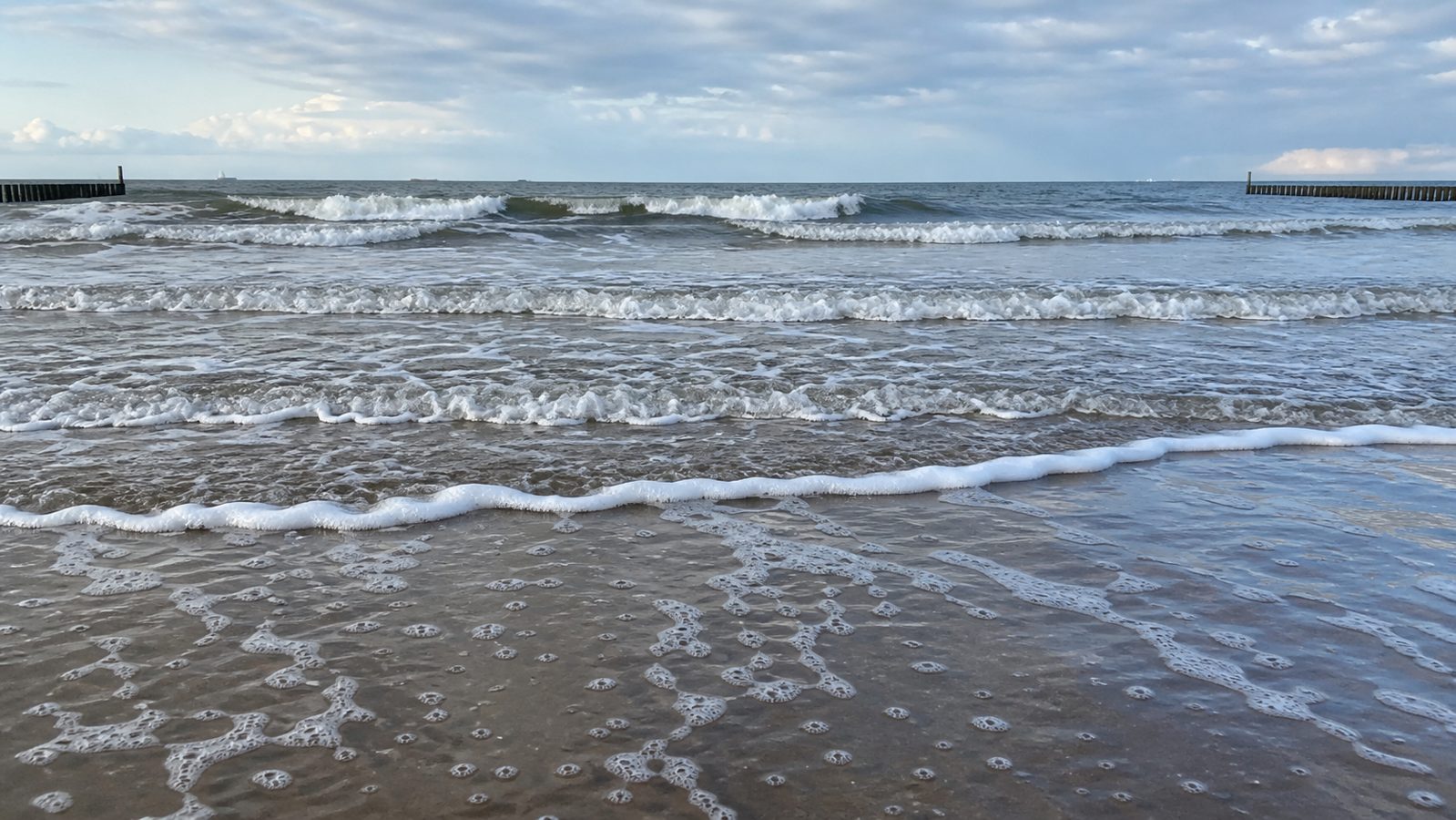 Lage foto van golflijnen en schuim op een Nederlands strand die golfperiode zichtbaar maken